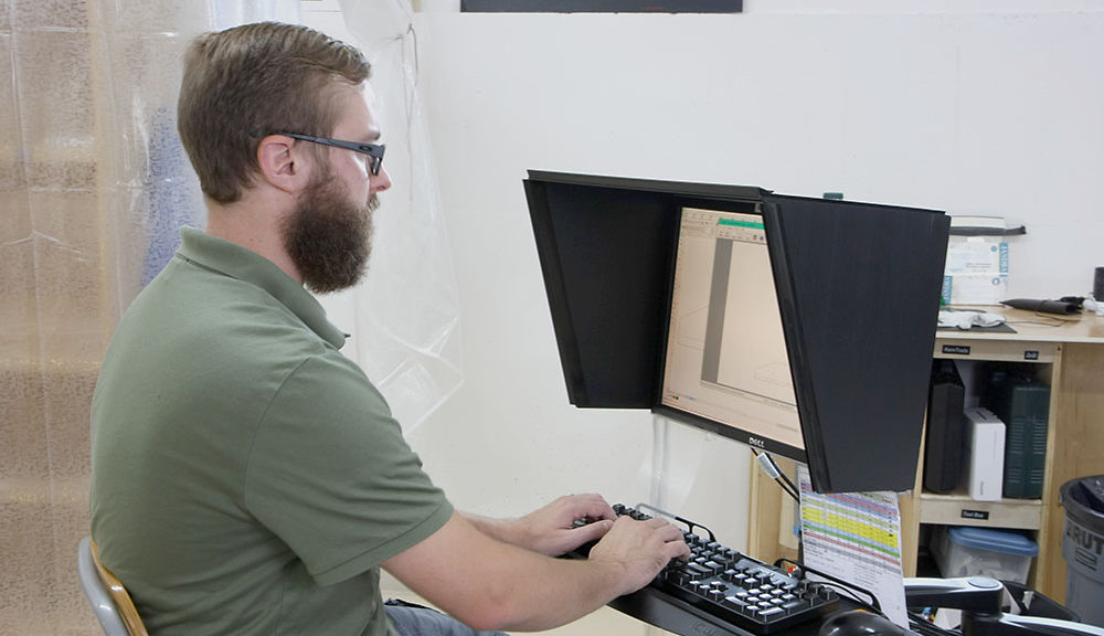 Man at a computer that has an indoor-outdoor monitor hood installed on it